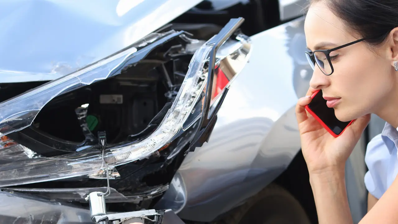 Frau telefoniert neben ihrem beschädigten Auto