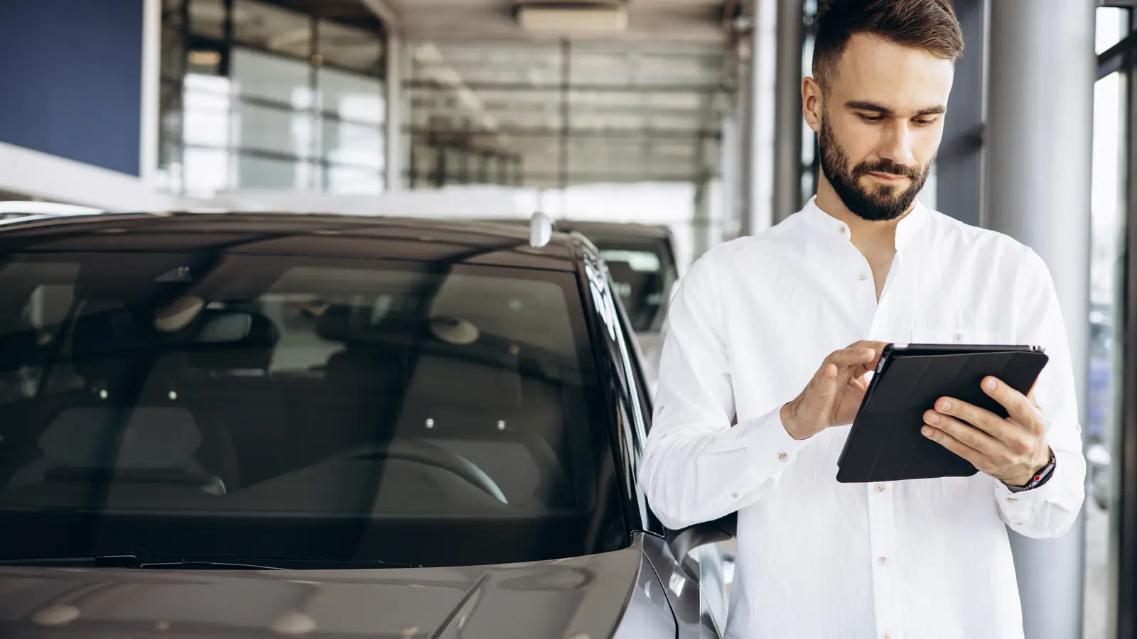 Mann mit Tablet neben einem Auto im Autohaus