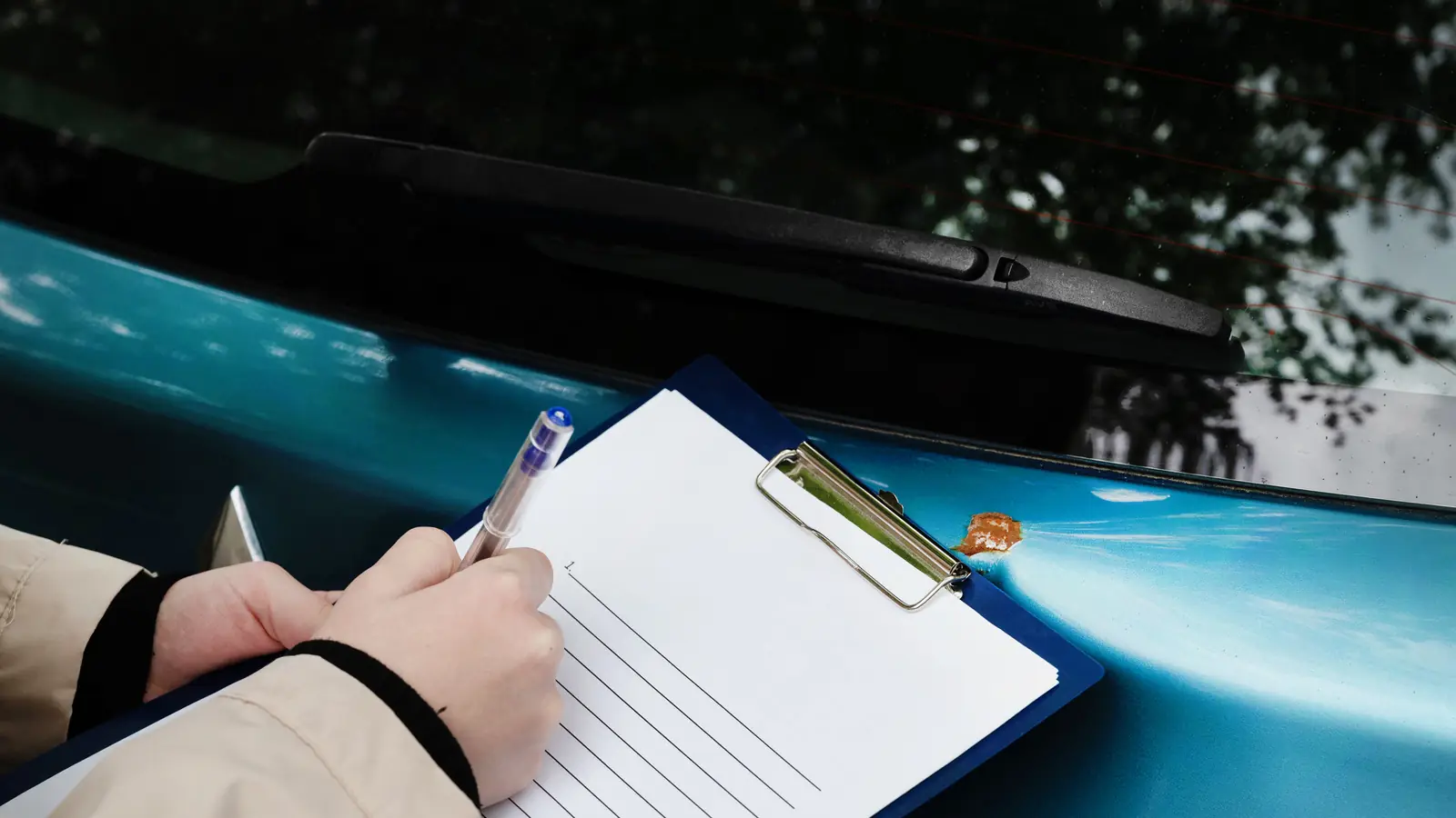 Klemmbrett mit Formular auf der eingedrückten Karosserie eines blauen Autos